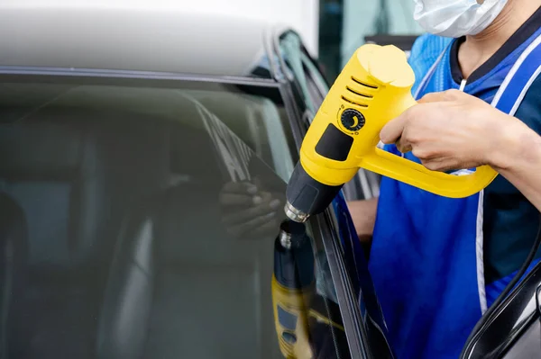 stock image Auto specialist worker hand blowing hot air dryer or hairdryer removing old car window film tint and installing the new one. Car front windscreen film removal and tinting installation