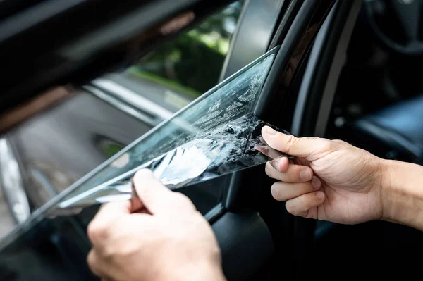 汽车侧窗膜的拆卸和着色安装 男性汽车专家手轻柔小心地从玻璃表面剥去旧的汽车保护膜 图库图片
