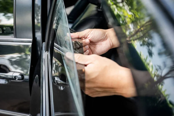 汽车侧窗膜的拆卸和着色安装 男性汽车专家手轻柔小心地从玻璃表面剥去旧的汽车保护膜 图库图片
