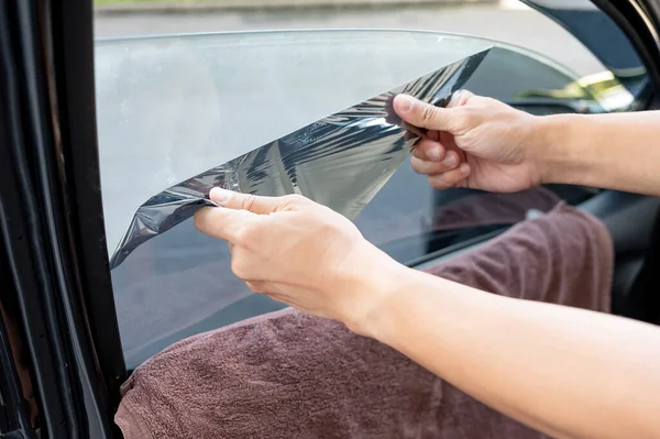 汽车侧窗膜的拆卸和着色安装 男性汽车专家手轻柔小心地从玻璃表面剥去旧的汽车保护膜 免版税图库图片