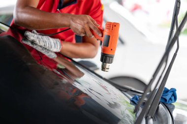 Otomobil uzmanı el fön makinesi ya da saç kurutma makinesi eski arabanın cam boyasını çıkarıp yenisini takıyor. Araba ön cam film kaldırma ve boyama kurulumu