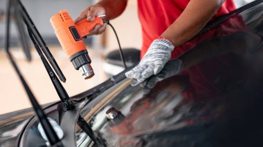 Otomobil uzmanı el fön makinesi ya da saç kurutma makinesi eski arabanın cam boyasını çıkarıp yenisini takıyor. Araba ön cam film kaldırma ve boyama kurulumu