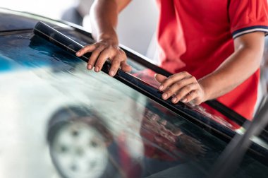 Erkek otomobil uzmanı el kamerasıyla ön cam yüzeyinde film çekiyor. Araba kenarı film kaldırma ve boyama kurulumu. 