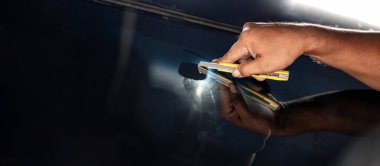 Arabanın yan tarafındaki film kaldırma ve boyama kurulumu. Erkek otomobil uzmanı el kesiciyi nazikçe tutuyor cam yüzeyinde arabanın ön camını kesiyor..