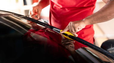 Arabanın yan tarafındaki film kaldırma ve boyama kurulumu. Erkek otomobil uzmanı el kesiciyi nazikçe tutuyor cam yüzeyinde arabanın ön camını kesiyor..