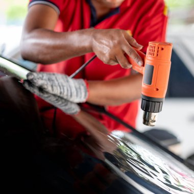 Otomobil uzmanı el fön makinesi ya da saç kurutma makinesi eski arabanın cam boyasını çıkarıp yenisini takıyor. Araba ön cam film kaldırma ve boyama kurulumu