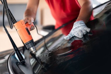 Otomobil uzmanı el fön makinesi ya da saç kurutma makinesi eski arabanın cam boyasını çıkarıp yenisini takıyor. Araba ön cam film kaldırma ve boyama kurulumu