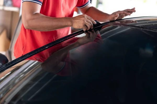 Auto specialist worker hand using squeegee blade or spatula installing car window film tint. Car side window film removal and tinting installation