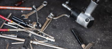 Bir sürü araba tamircisi var. Garajda araba tamiri ve lastik değiştirme. Uzun iğne burun pensesi, anahtar, çekiç, tornavida ve otomatik tamirhanenin beton zemininde pnömatik anahtar.