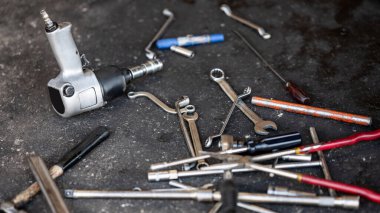 Bir sürü otomatik mekanik alet. Garajda araba tamiri ve lastik değiştirme. Pnömatik anahtar, anahtar, çekiç, tornavida ve oto tamirhanesinin beton zeminindeki diğer mekanik çalışma aletleri.
