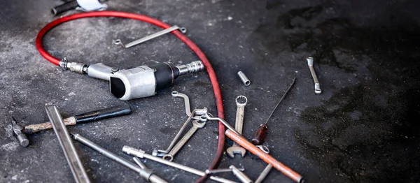 Many auto mechanic tools. Car suspension fixing and tire changing in the garage. Pneumatic wrench, spanner, hammer, screwdriver and other mechanical work tools on concrete floor in auto repair shop