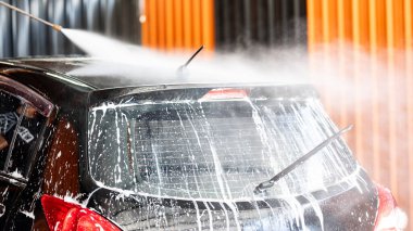 Otomobil yıkama servisi. Araba bakımı konsepti. Araba yıkama istasyonunun çatısındaki köpüğü temizlemek için yüksek basınçlı su sıkma uzmanı.