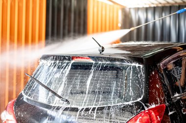 Otomobil yıkama servisi. Araba bakımı konsepti. Araba yıkama istasyonunun çatısındaki köpüğü temizlemek için yüksek basınçlı su sıkma uzmanı.