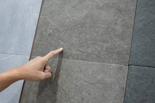 Male hand pointing at stone tile texture choosing sample material for floor finishing in home design store. Home improvement concept