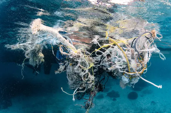 Abandoned debris fishing net or ghost net and plastic garbages in the sea. Clean up the ocean by collecting waste. Save the ocean and underwater world from trash pollution. Environmental conservation