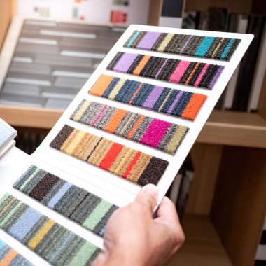 Tasarımcı elinde halı kumaş kumaşı koleksiyonu tutuyor. Müşteri ev tasarımı mağazasında iç katalogdan renk örneği seçiyor
