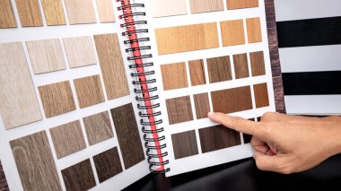 Tasarımcı el malzeme örnek kataloğundaki ahşap lamine kumaş koleksiyonunu işaret ediyor. Müşteri mobilya yapımı ya da iç mimarisi için doğal ahşap dokuyu seçiyor.