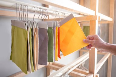 Kumaş kumaşından sarı kumaş parçası seçen stilist el. Döşeme örneği koleksiyonu vitrin rafında asılı duruyor. Ev iç tasarımı ve mobilya dekorasyonu için tekstil endüstrisi