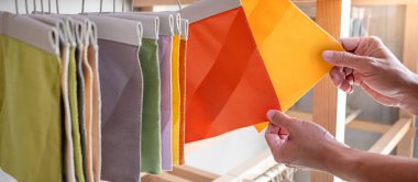 Kumaş kumaşındaki kumaş parçalarını karşılaştıran stilist el. Döşeme örneği koleksiyonu vitrin rafında asılı duruyor. Ev iç tasarımı ve mobilya dekorasyonu için tekstil endüstrisi