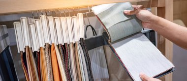 Tasarımcı el kumaş kumaşından kumaş parçaları seçiyor. Döşeme örneği koleksiyonu vitrin rafında asılı duruyor. Ev iç tasarımı ve mobilya dekorasyonu için tekstil endüstrisi