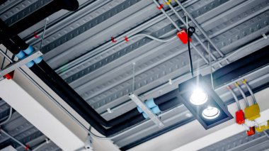 Spotlight lambası elektrik kablolarının altında asılı renkli bağlantı kutusuyla ve modern binanın metalik tavanına boru hattı döşenmiş. Boru ve tesisat sistemi için uygun.