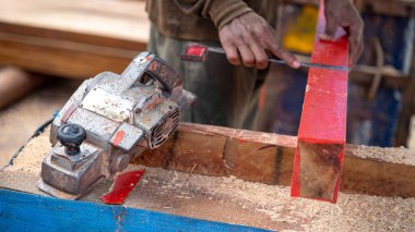 Marangoz eli arkada kereste karelerken tezgahın üzerinde kırsal elektrik planörü. İnşaat alanında ahşap kalas döşeyen bir ahşap işçisi. Marangozluk işi aracı ve kereste endüstrisi konsepti