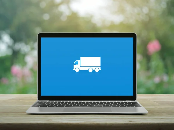 Delivery truck flat icon on modern laptop computer screen on wooden table over blur pink flower and tree in garden, Business transportation online service concept