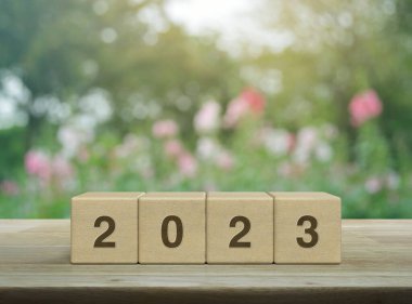 2023 letter on wood block cubes on wooden table over blur pink flower and tree in garden, Happy new year 2023 cover concept clipart