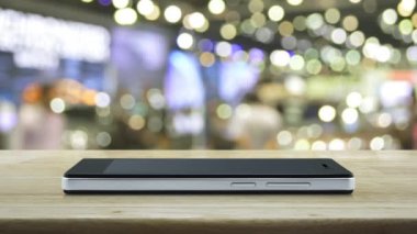 Hediye kutusu mutlu yıllar 2023 modern akıllı cep telefonu ekranındaki düz simge bulanık ışık ve alışveriş merkezinin gölgesi üzerindeki ahşap masa, iş yeni yılı mutlu yıllar 2023 çevrimiçi dükkan konsepti