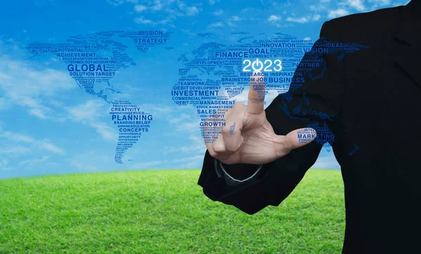 Businessman pressing 2023 start up business icon with global words world map over green grass field with blue sky, Happy new year 2023 global business start up concept, Elements of this image furnished by NASA