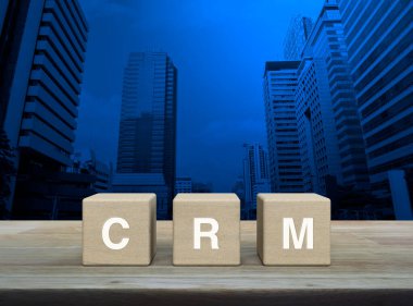 Ahşap blok küplere yazılmış CRM mektubu modern ofis kulesi ve gökdelen üzerindeki ahşap masa, Müşteri İlişkileri Yönetimi konsepti