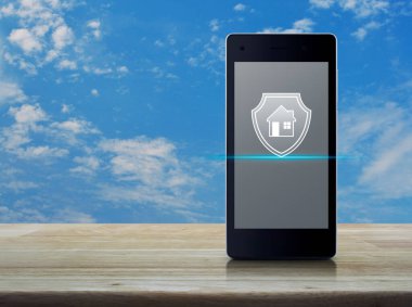 Beyaz bulutlu ahşap gökyüzü, iş yeri sigortası ve güvenlik online konsepti ile ahşap masa üzerinde modern akıllı cep telefonu ekranı simgesi ile ev