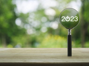 2023 tahta masanın üzerinde büyüteçle parktaki bulanık yeşil ağacın üzerinde düz bir ikon oluşturun. Yeni yıl 2023 kapak konsepti mutlu yıllar.