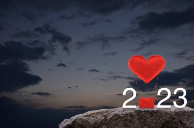 Kırmızı Kumaş Kalp, 2023 beyaz yazılı hava balonunu sever. Gün batımında gökyüzünde kaya dağında. Mutlu yıllar ve Sevgililer Günü 2023 konsepti.