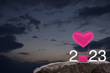 Pink fabric heart love air balloon with 2023 white text on rock mountain over sunset sky, Happy New Year and Valentines Day 2023 Concept