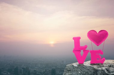 Pink love alphabet and fabric heart balloon on rock mountain over aerial view of cityscape at sunset, vintage style, Valentines day concept clipart