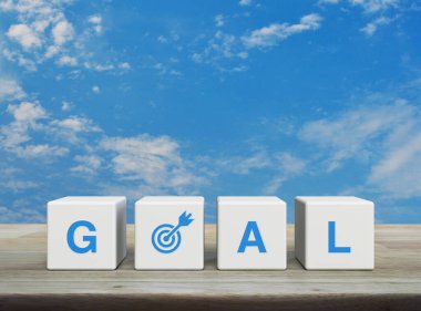 Goal icon on white block cubes on wooden table over blue sky with white clouds, Business success concept