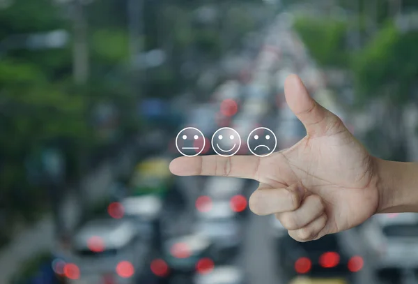 Excellent smiley face rating icon on finger over blur of rush hour with cars and road in city, Business customer service evaluation and feedback rating concept