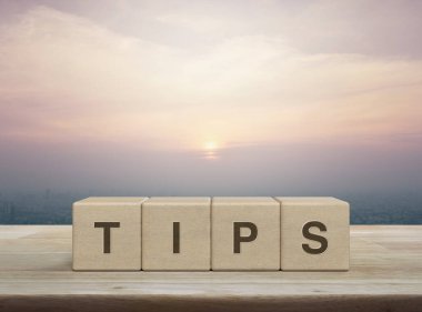 Tahta blok küplere yazılmış TIPS mektubu şehir kulesinin üzerindeki ahşap masa ve günbatımında gökdelen, klasik tarz, müşteri hizmetleri ve destek konsepti.