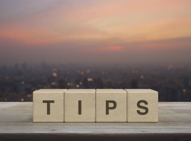 Tahta bloktaki küplere yazılmış TIPS mektubu ahşap masa üzerindeki bulanık şehir manzarası gün batımında, iş dünyası müşteri hizmetleri ve destek kavramı.