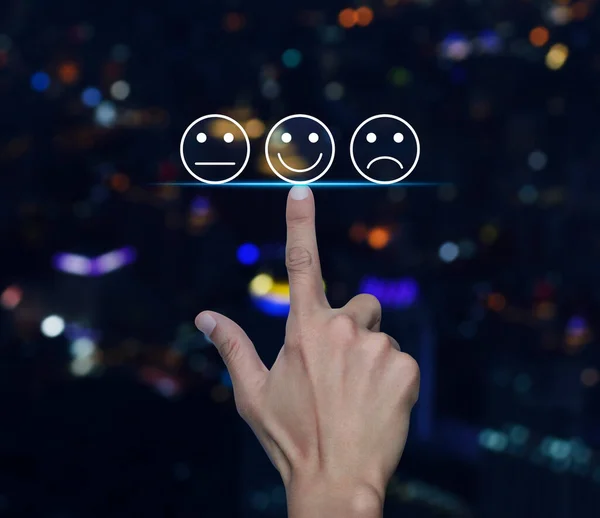Hand pressing excellent smiley face rating icon over blur colorful night light modern city tower and skyscraper, Business customer service evaluation and feedback rating concept