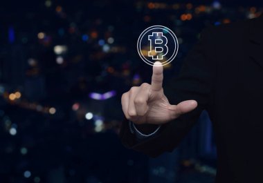 İş adamı bulanık gece lambası şehir kulesi ve gökdelen üzerine Bitcoin simgesi bastırıyor, bitcoin konseptini seçiyor