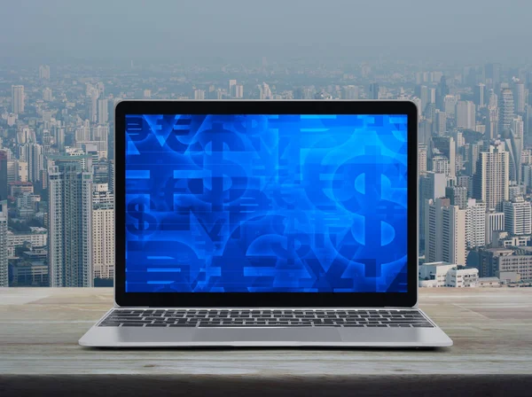 现代笔记本电脑屏幕上的金融货币符号出现在城市塔楼和摩天大楼上方的木制桌子上 — 图库照片