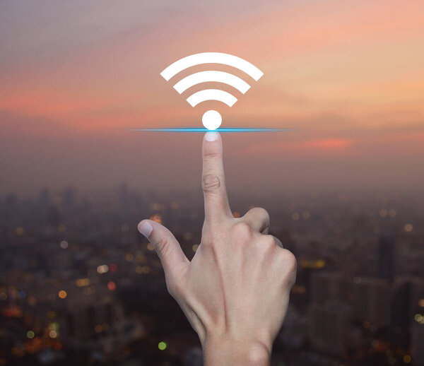 Hand pressing wi-fi flat icon over blur of cityscape on warm light sundown, Technology internet communication concept