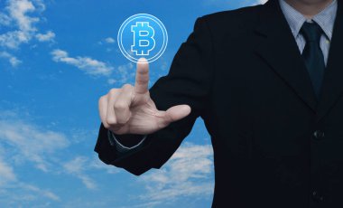 İş adamı beyaz bulutlu mavi gökyüzü üzerine Bitcoin simgesi bastırıyor, bitcoin konseptini seçiyor