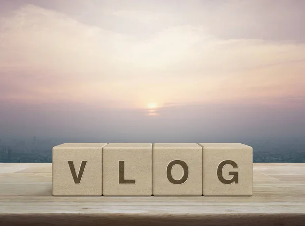 stock image Vlog letter on wood block cubes on wooden table over city tower and skyscraper at sunset, vintage style, Vlog video marketing concept