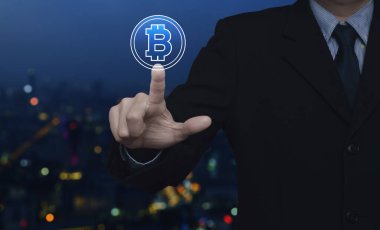 İş adamı bulanık gece lambası şehir kulesi ve gökdelen üzerine Bitcoin simgesi bastırıyor, bitcoin konseptini seçiyor