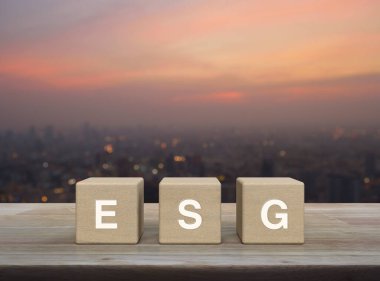 Tahta küpler üzerine ESG harfi. Şehir manzarası bulanık. Gün batımında, Çevresel Sosyal Yönetim kavramı.