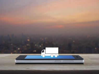 Kamyon düz simgesi modern akıllı cep telefonu ekranı ahşap masa üzerinde sıcak gün batımı bulanık şehir manzarası, iş ulaşımı çevrimiçi servis konsepti