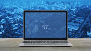 Soru işareti simgesi simgesi modern dizüstü bilgisayarlı ahşap masa üzerinde şehir kulesi, sokak, gökdelen, iş dünyası müşteri hizmetleri ve çevrimiçi konsept desteği